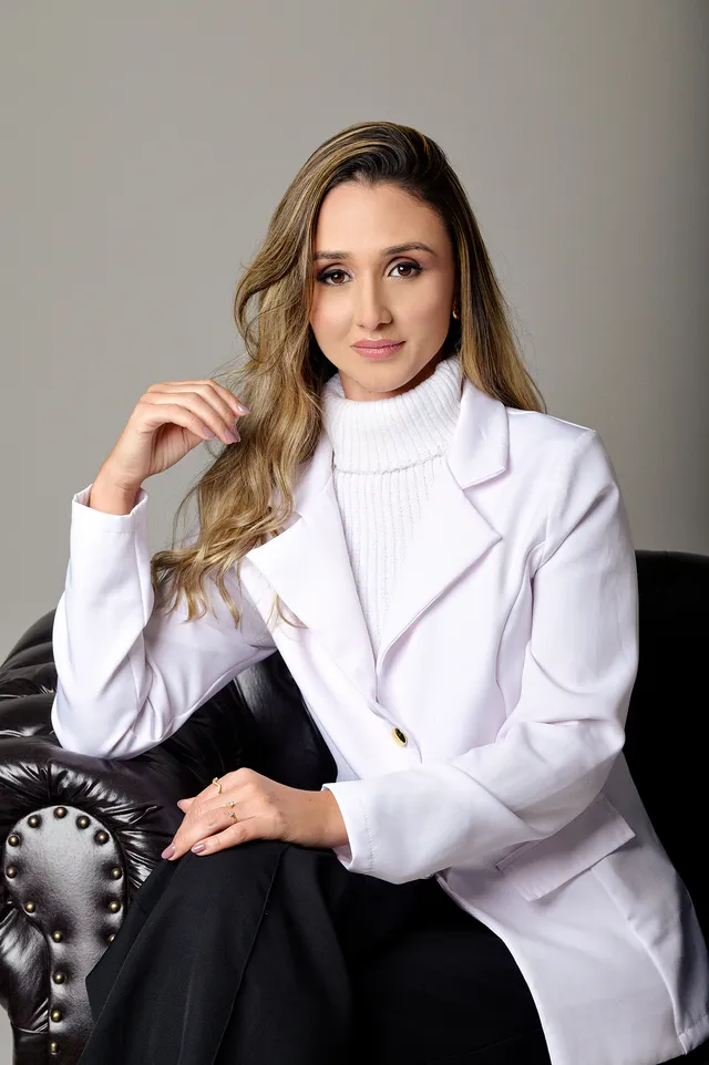 Mulher de blazer branco sentada em poltrona escura, em estúdio
