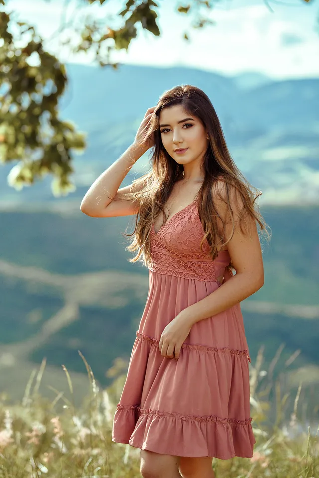 Mulher de vestido rosa em campo aberto, com montanhas ao fundo