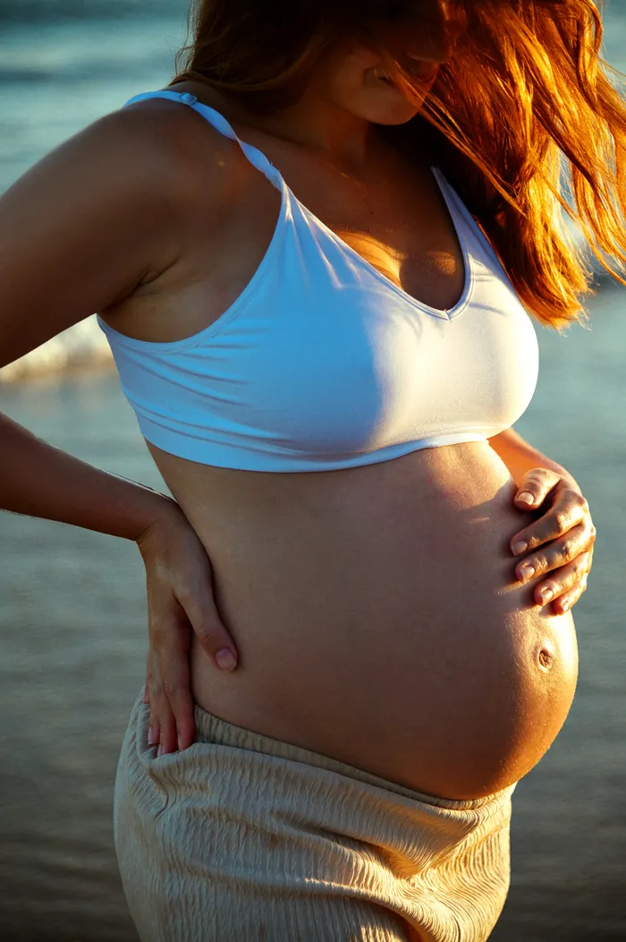 Gestante à beira-mar no fim da tarde, com as mãos apoiadas na barriga